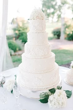 a white wedding cake sitting on top of a table next to wine glasses and flowers