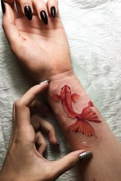 a woman's arm with a goldfish tattoo on it