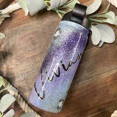 a purple and blue water bottle sitting on top of a wooden table next to leaves