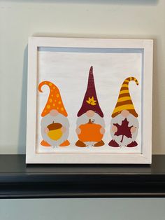 three little gnomes are sitting in front of a white framed art print on the wall