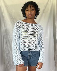 a woman standing in front of a white backdrop wearing short shorts and a crocheted sweater