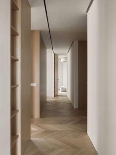 an empty hallway with wood flooring and shelving on either side, leading to a bed