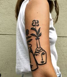 a woman with a tattoo on her arm holding a vase and flowers in front of her face