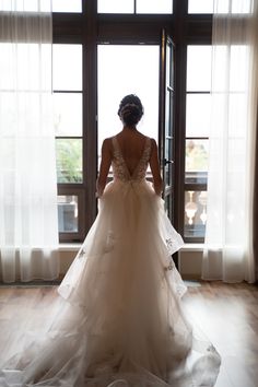 the back of a bride's dress as she stands in front of a window