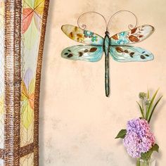 a vase filled with purple flowers next to a wall mounted dragonfly decoration on the side of a wall