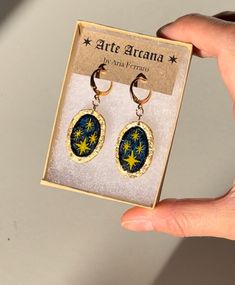 a pair of earrings with stars on them are in a box and it is being held by a hand