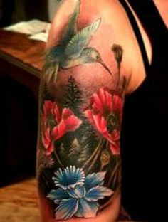 a woman's arm with a humming bird and flowers on it