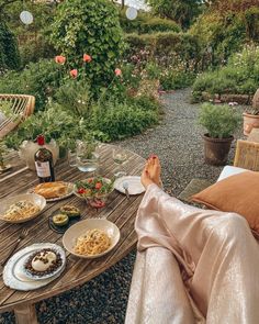 a woman sitting at a table with food and wine in front of her, looking out onto the garden