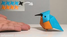 an origami bird sitting on top of a table next to someone's hand