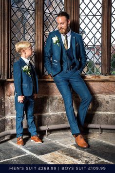 a young boy in a blue suit standing next to an older man