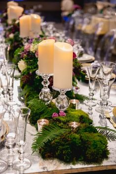 the table is set with candles, moss and glassware for an elegant touch to the centerpieces