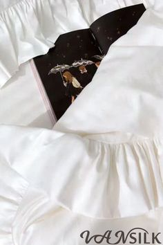 an open book laying on top of a white comforter covered in ruffles