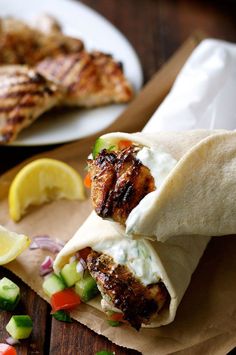 two pita breads with chicken and vegetables on the side next to some sliced lemon wedges