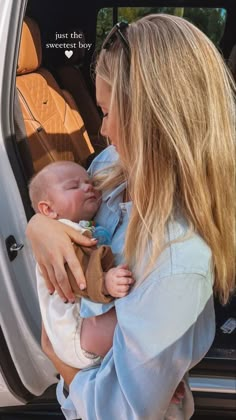 a woman holding a baby in her arms and looking into the back of a car