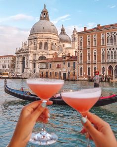 two people holding wine glasses in front of a gondola on the water with buildings in the background