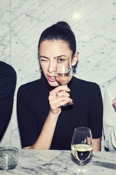 a woman holding a glass of wine in front of her face while sitting at a table