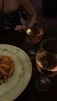 a white plate topped with pasta next to two glasses of wine