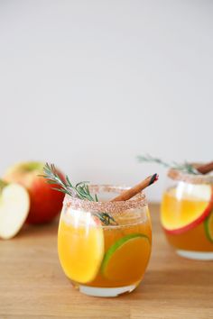 two glasses filled with apple cider on top of a wooden table