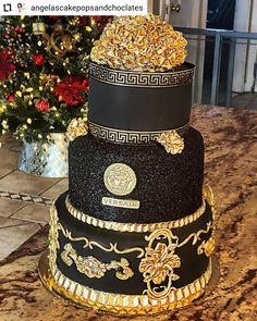 a three tiered black and gold wedding cake on a table with a christmas tree in the background