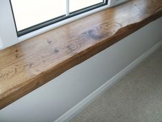 a wooden window sill sitting in front of a window next to a white wall