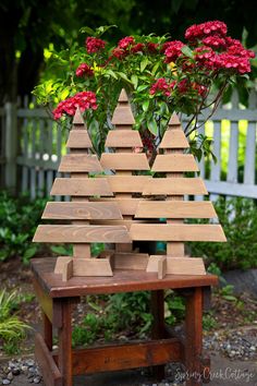 a small wooden christmas tree sitting on top of a table next to flowers and a fence