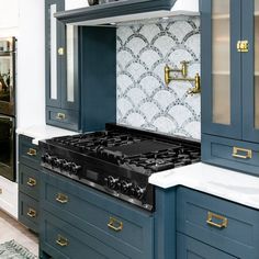 a kitchen with blue cabinets and gold pulls on the stove top, marble counter tops