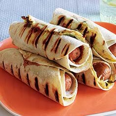 three hotdogs are on a plate next to a glass of water and an orange napkin