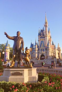 a statue of walt and mickey mouse in front of a castle