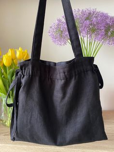 a black bag sitting on top of a wooden table next to yellow and purple flowers