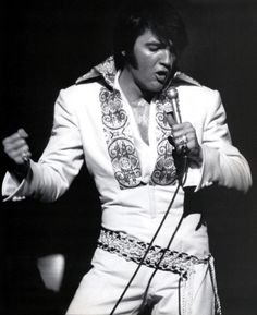 elvis presley singing into a microphone with his hands in the air while wearing white pants