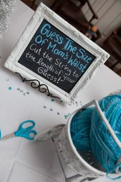 a table topped with balls of yarn next to a chalkboard sign that says guess the size of mom's most