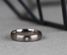 a wedding band with a single diamond sits on the floor next to a metal rack