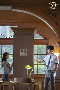 a boy and girl are standing in front of a desk with a lamp on it