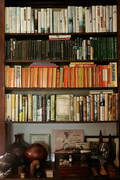 a bookshelf filled with lots of books on top of a wooden table next to a vase