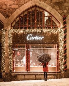 a woman holding an umbrella standing in front of a store with christmas lights on the windows