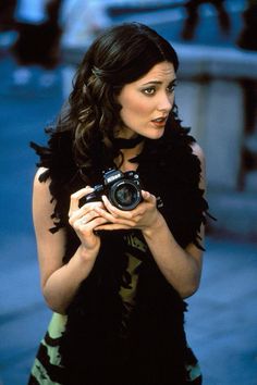 a woman holding a camera and looking at the screen in front of her is wearing a black feathered dress