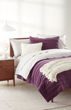 a bed with purple and white comforters in a bedroom next to a night stand