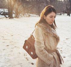 a woman walking in the snow carrying a purse