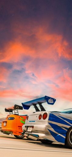 an orange and blue race car driving down the road in front of a colorful sky