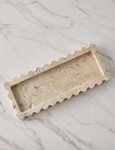 a white marble tray with scalloped edges on a marble countertop or floor