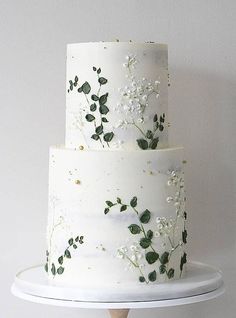 a three tiered cake with white flowers and green leaves