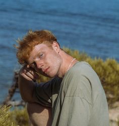 a man with red hair is leaning on the edge of a cliff by the ocean