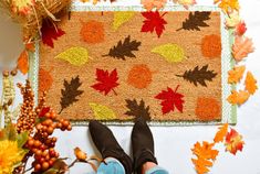 a person standing in front of a door mat with autumn leaves on it