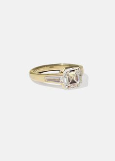 a yellow gold ring with an emerald and baguette cut diamond in the center