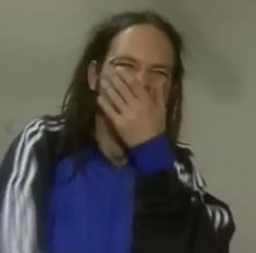 a man with long hair covers his face while standing in front of a white wall