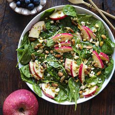 a white bowl filled with spinach, apples and blueberries on top of a wooden table