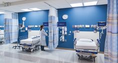 a hospital room with beds, carts and clocks on the walls in blue paint scheme