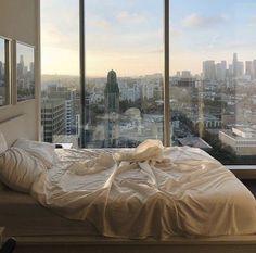 an unmade bed in front of a large window overlooking cityscape and skyscrapers