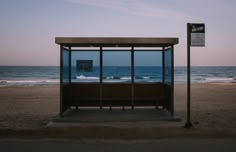 a bus stop sitting on top of a sandy beach next to the ocean at dusk