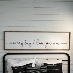 a bed with black and white pillows in front of a sign that says, every day i love you more